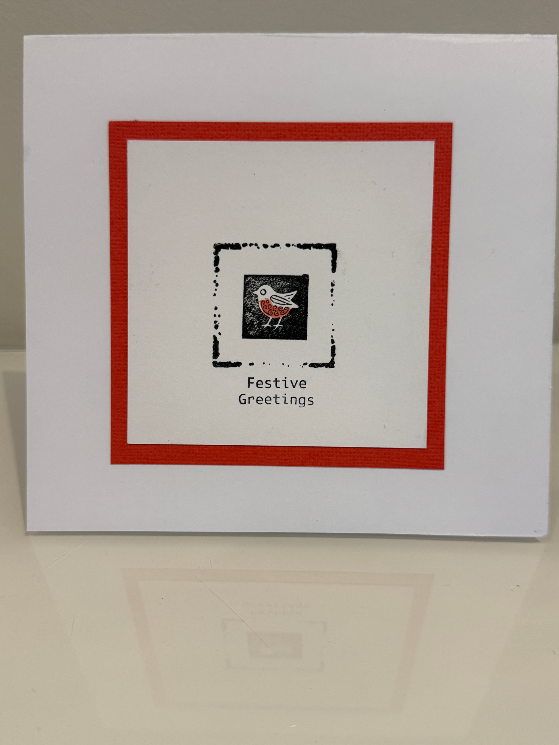 White card with red border and black square featuring a design and text 'Festive Greetings' on a beige background.