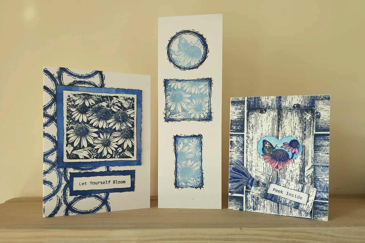 Three handmade greeting cards with blue and white floral and butterfly designs, displayed on a wooden surface against a beige background.