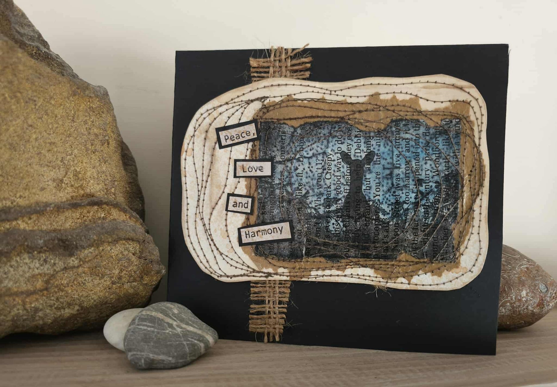 Artistic piece with text and silhouette on a black background, surrounded by stones.