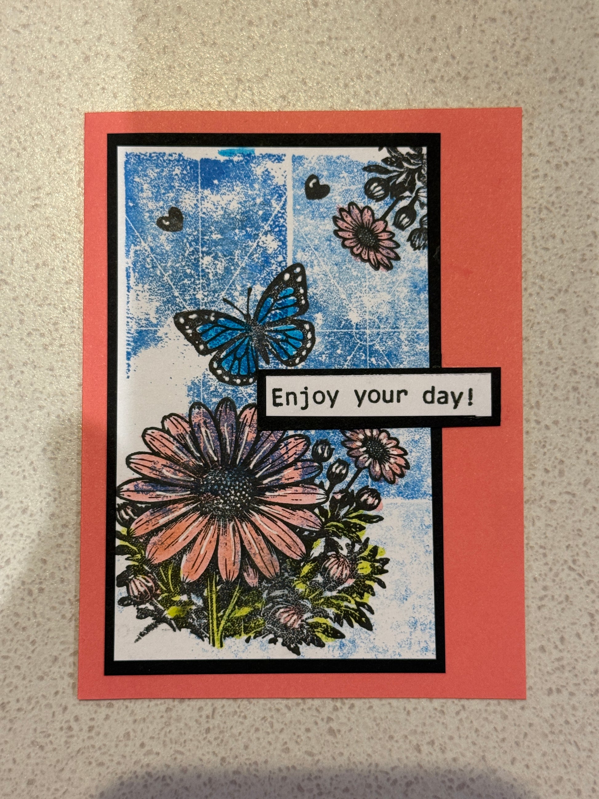 Greeting card with floral design and 'Enjoy your day!' text on a textured surface