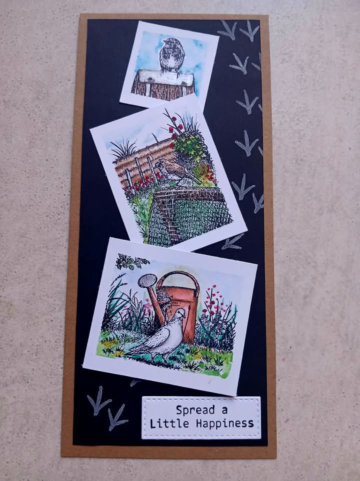 A handmade greeting card featuring three illustrated garden-themed photo inserts on a dark navy background with white bird silhouettes and the text 'Spread a Little Happiness' at the bottom, photographed on a beige textured surface.