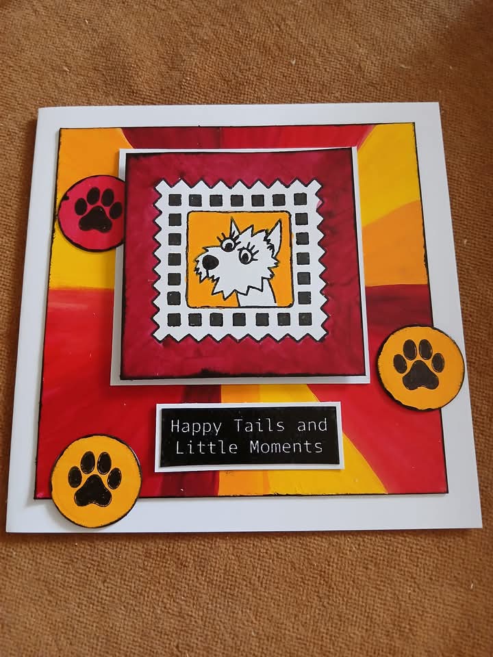 A handmade greeting card featuring a West Highland White Terrier illustration, colorful abstract red, orange, and yellow background shapes, three paw print stickers, and the text 'Happy Tails and Little Moments' on a brown fabric background.