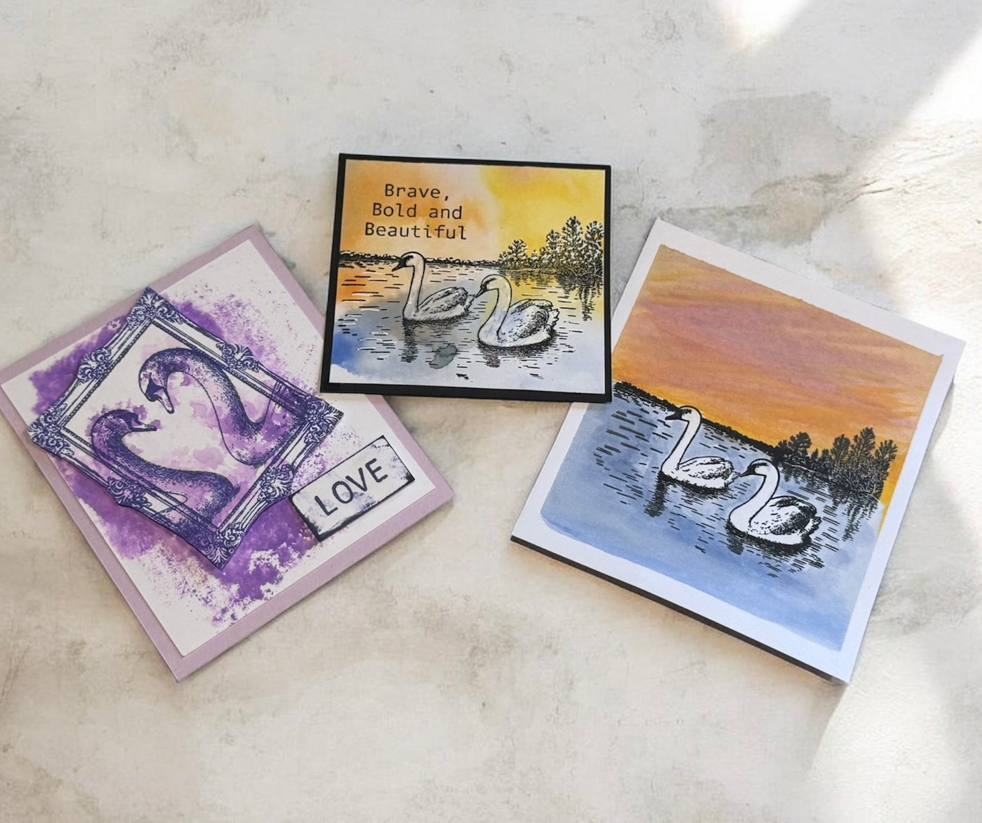 Four greeting cards with swan designs on a textured surface