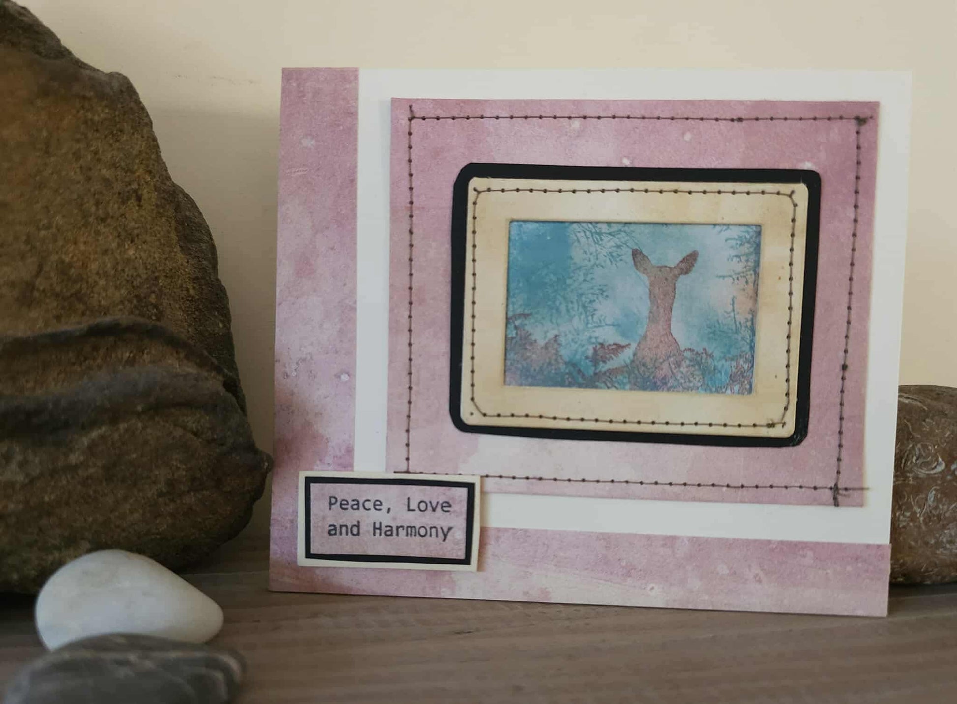 Card with a deer illustration and 'Peace, Love and Harmony' text on a textured surface.