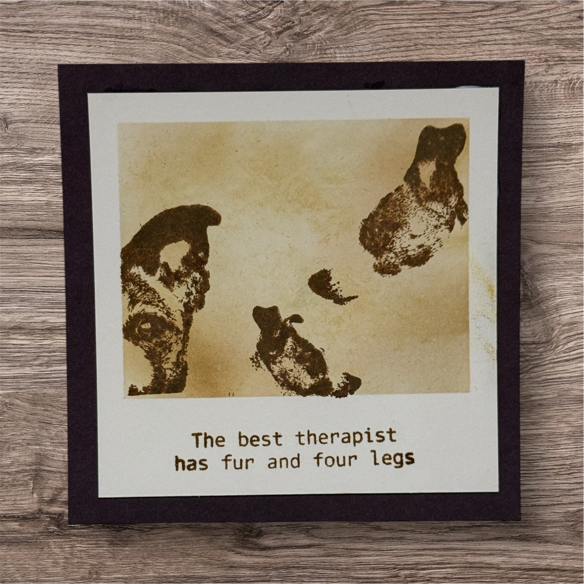 Framed print with paw prints and text 'The best therapist has fur and four legs' on a wooden surface.