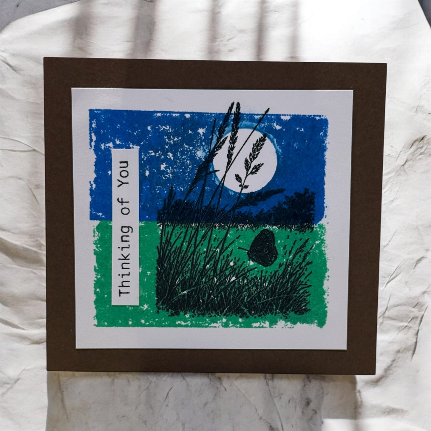 Greeting card with moon and grass design on a textured fabric background