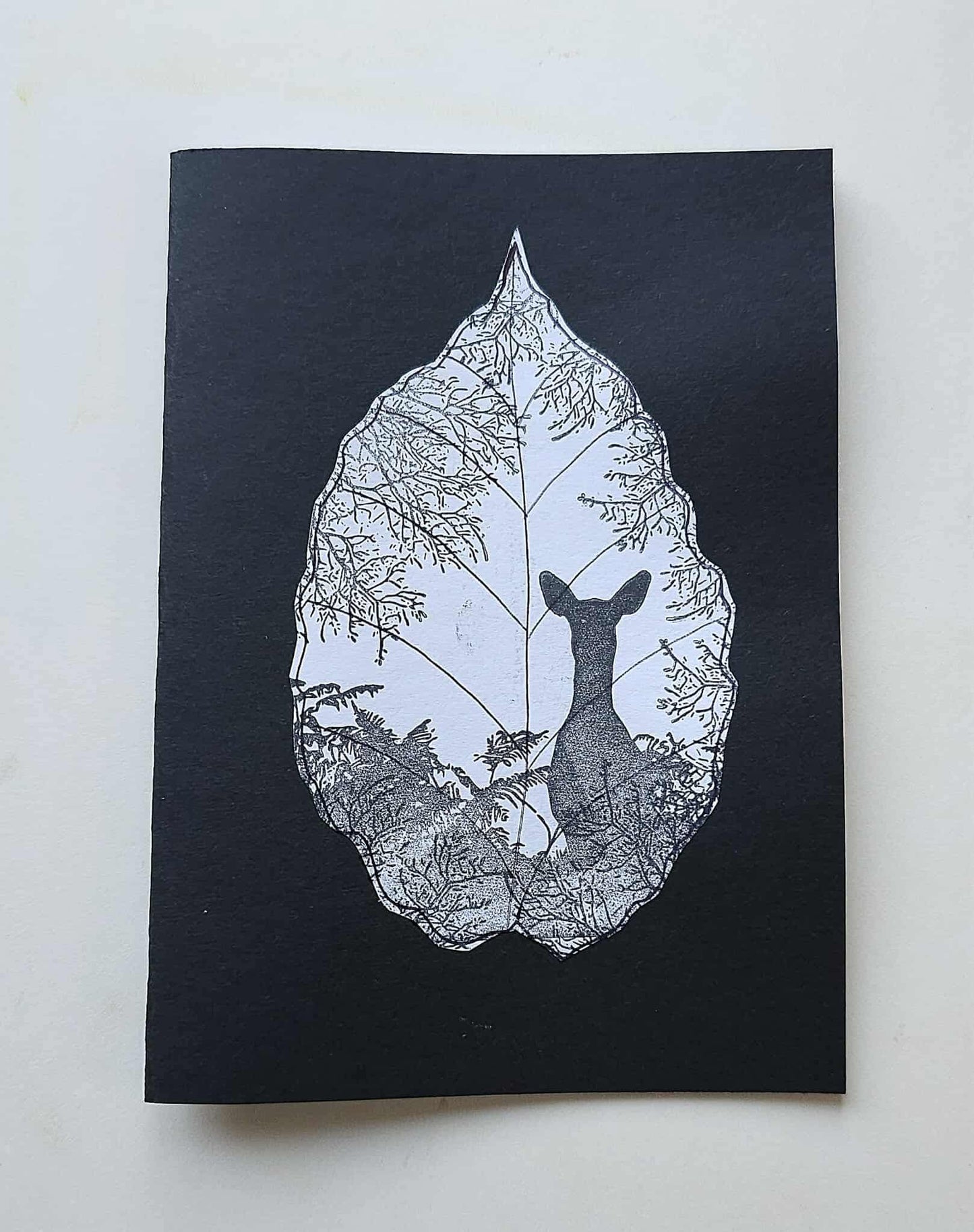 Black notebook with a white leaf design featuring a deer, on a light gray background