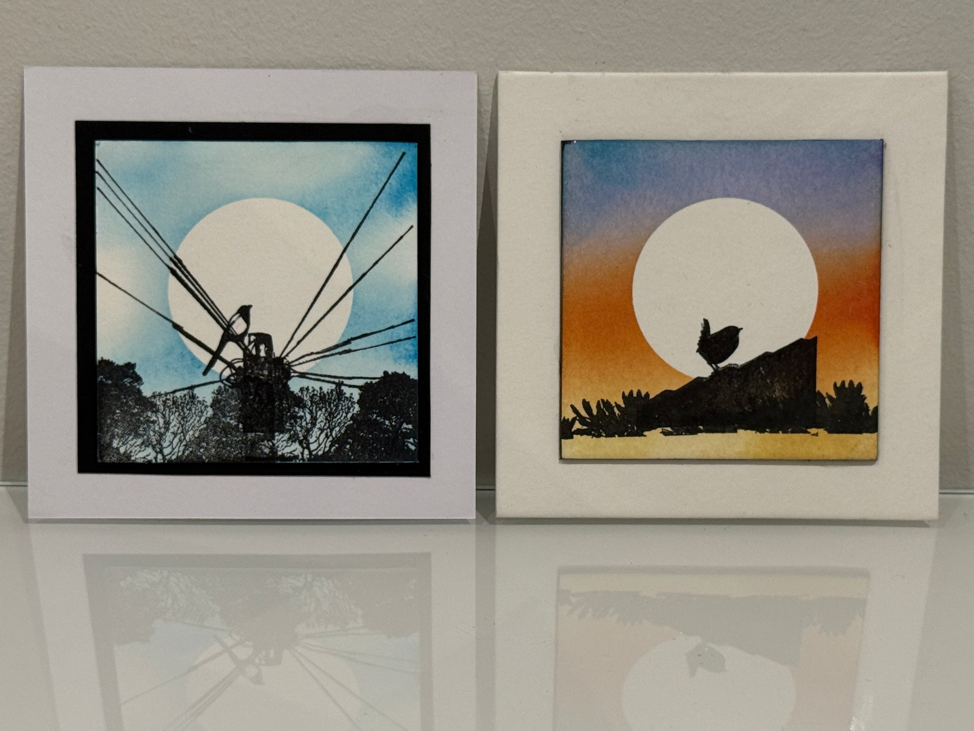 Two framed artworks with silhouettes against a sunset and moonlit sky.