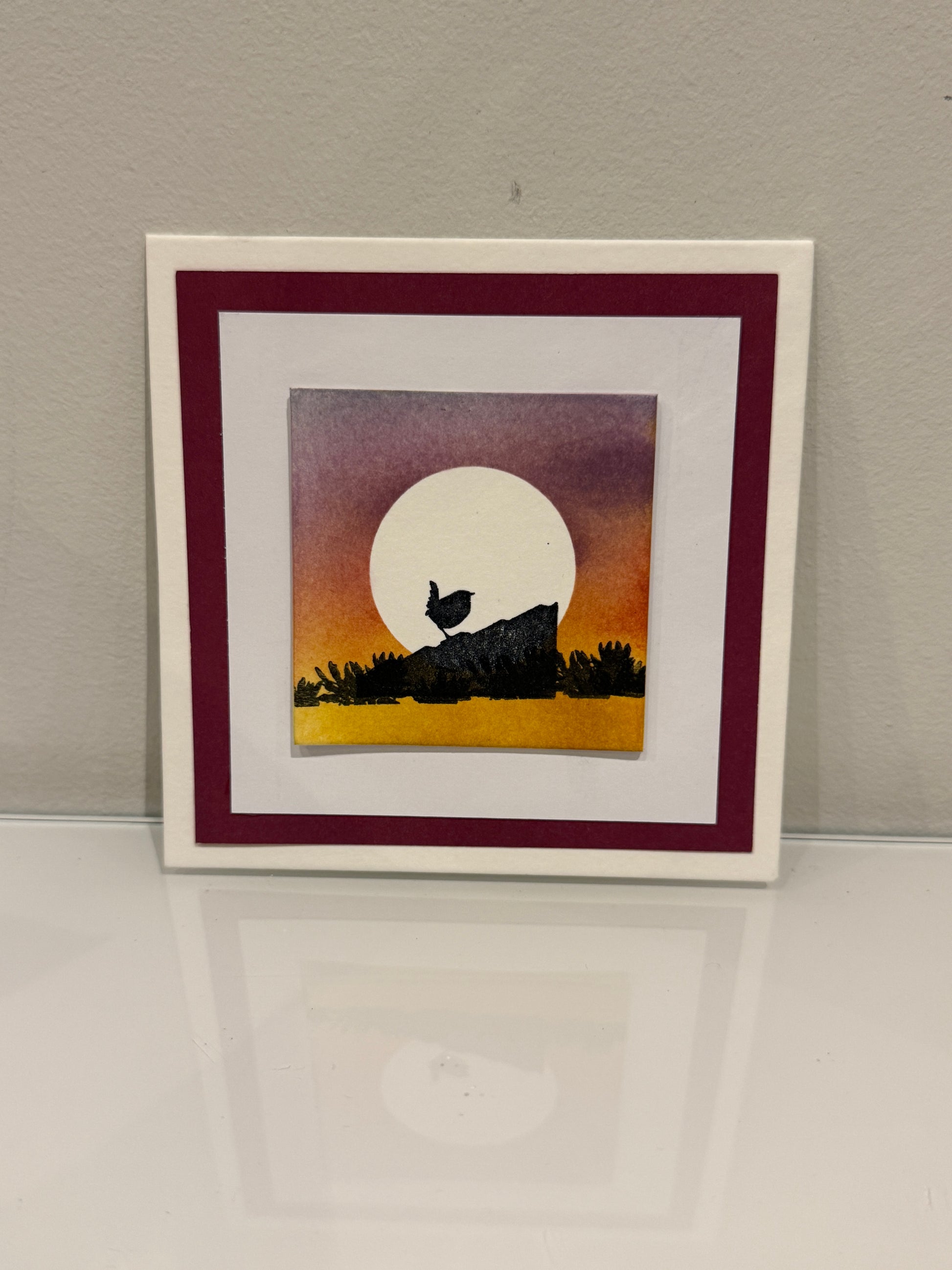 Framed artwork of a bird silhouette against a sunset sky on a wall.