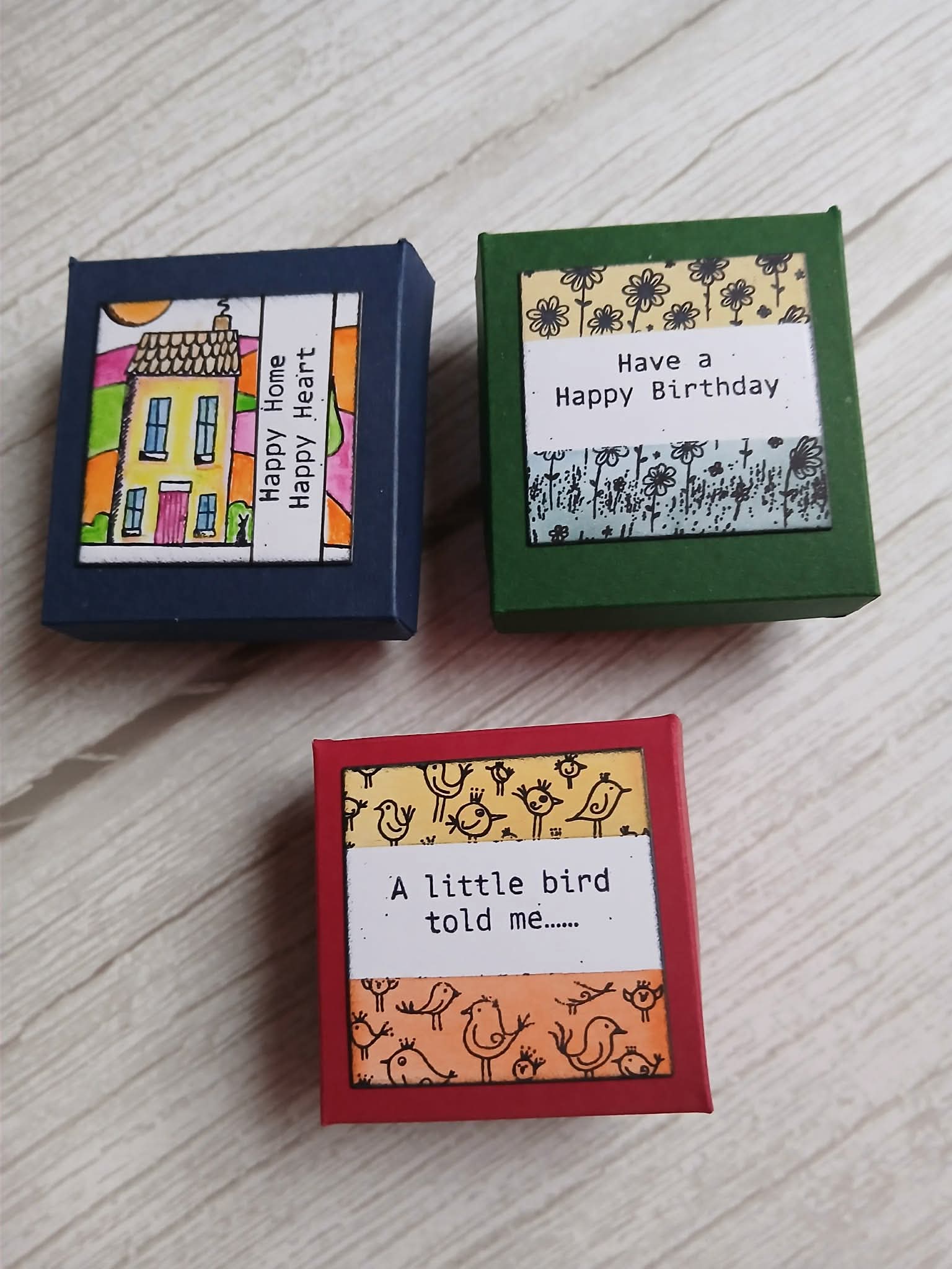 Three small decorative boxes with colorful labels on a wooden surface