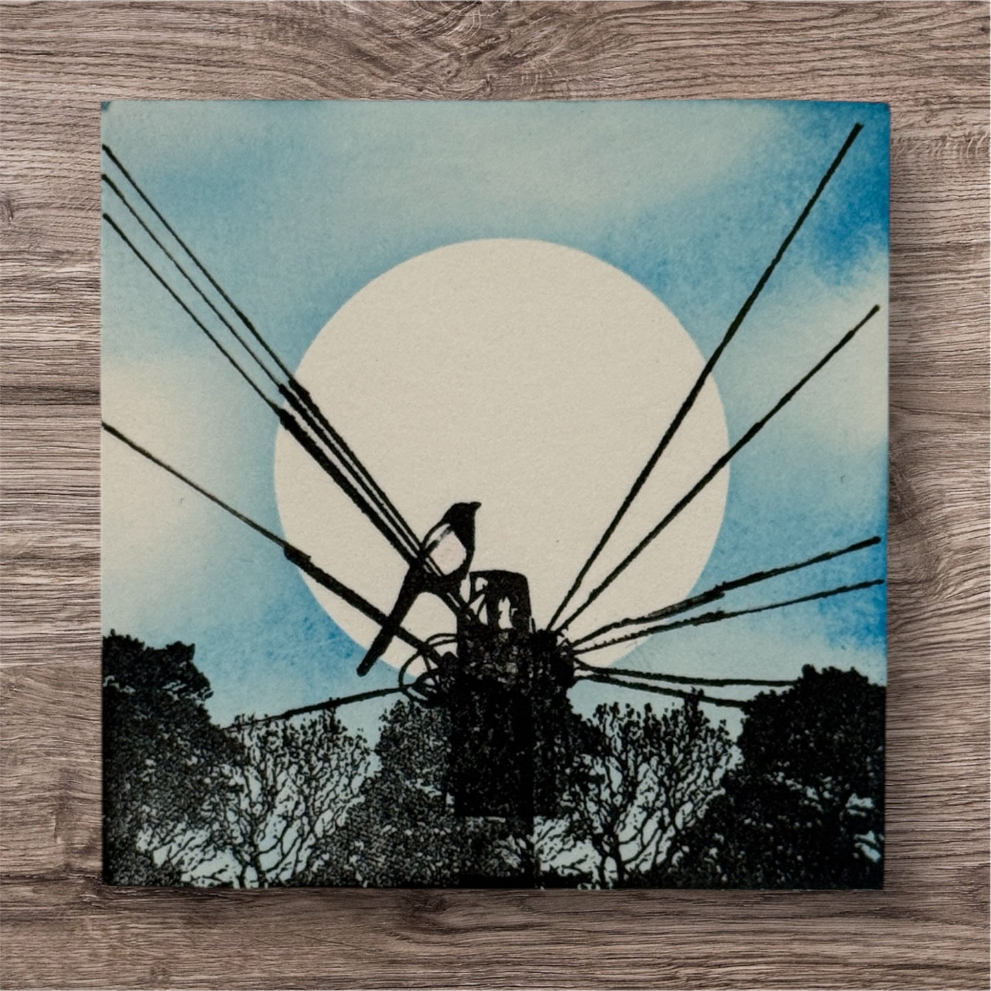 Artistic depiction of a windmill against a blue sky with a white circle, on a wooden surface.
