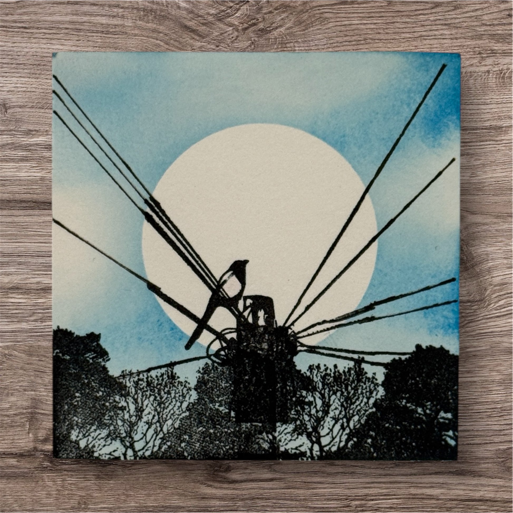 Artistic depiction of a windmill against a blue sky with a white circle, on a wooden surface.