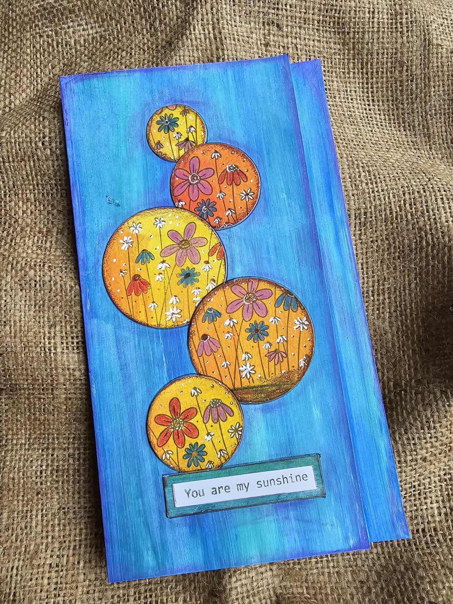 Colorful card with floral designs and 'You are my sunshine' text on a textured fabric background