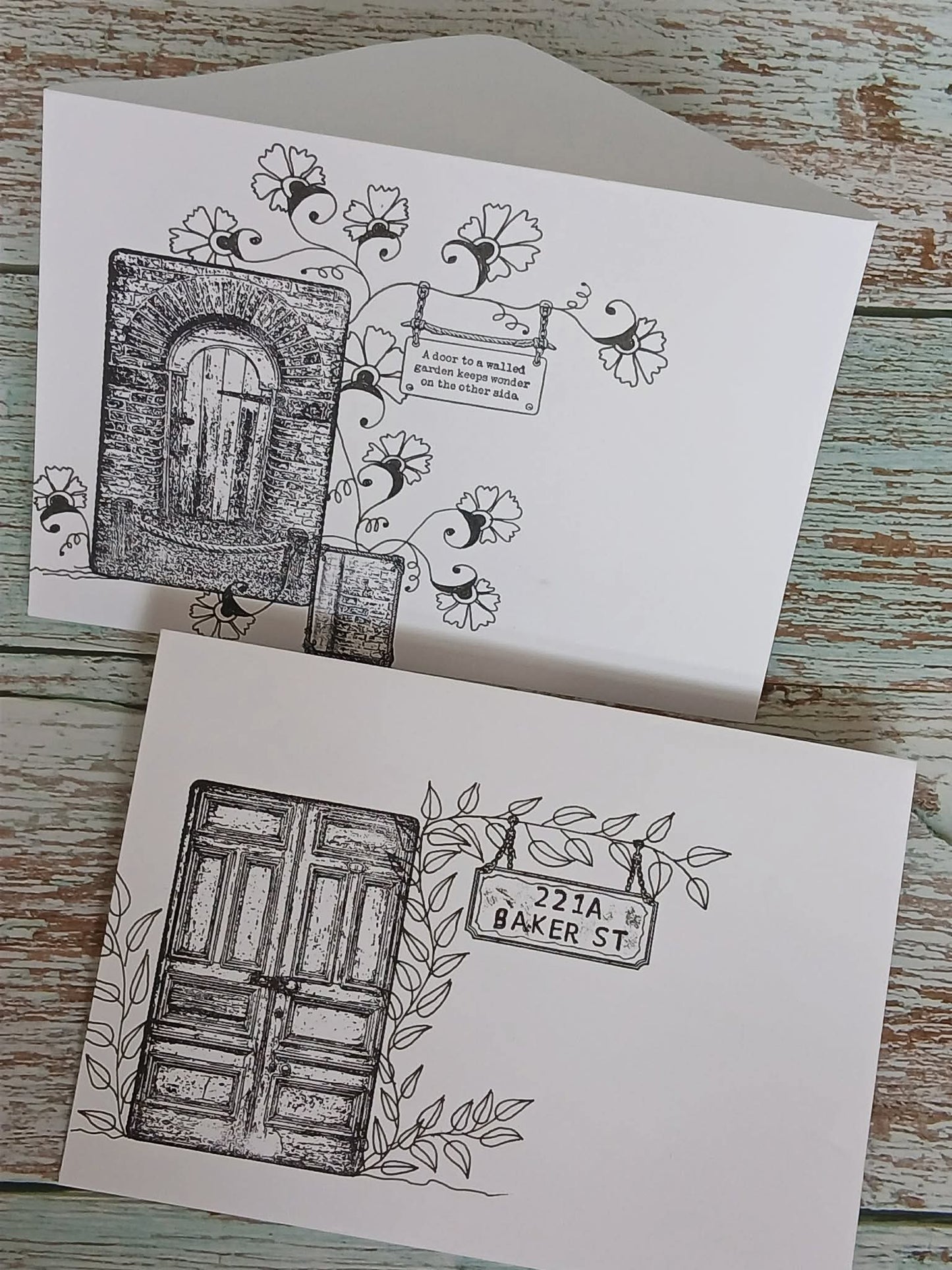 Two greeting cards with black and white illustrations of doors and street signs on a wooden surface.