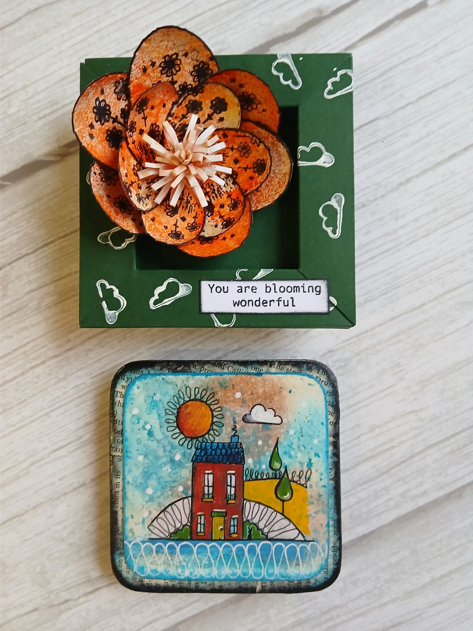 Decorative box with a flower-shaped object and a small artwork on a wooden surface