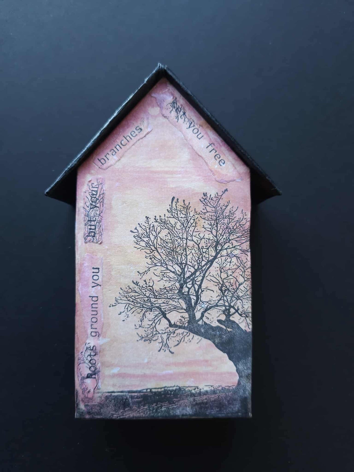 House-shaped decorative item with a tree design and text on a dark background