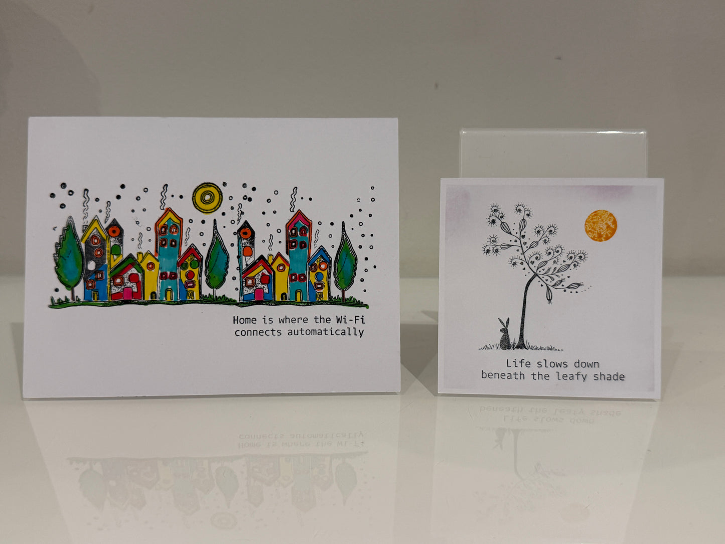 Two greeting cards with illustrations and text on a reflective surface.