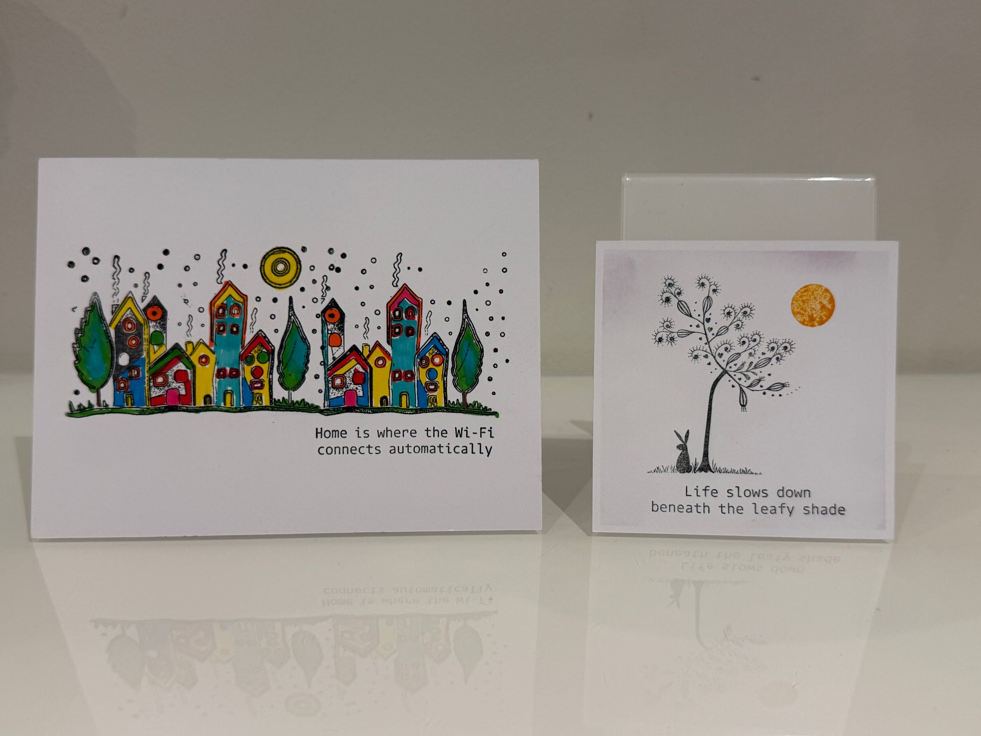 Two greeting cards with illustrations and text on a reflective surface.