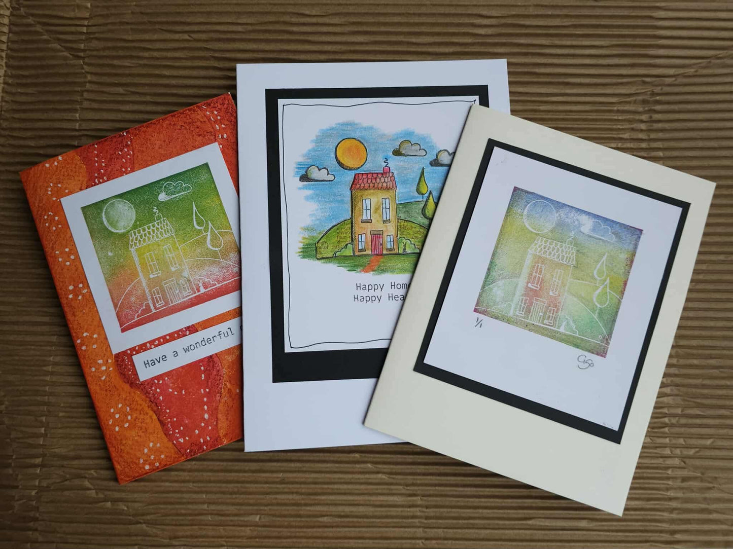 Three greeting cards with artistic designs on a wooden surface
