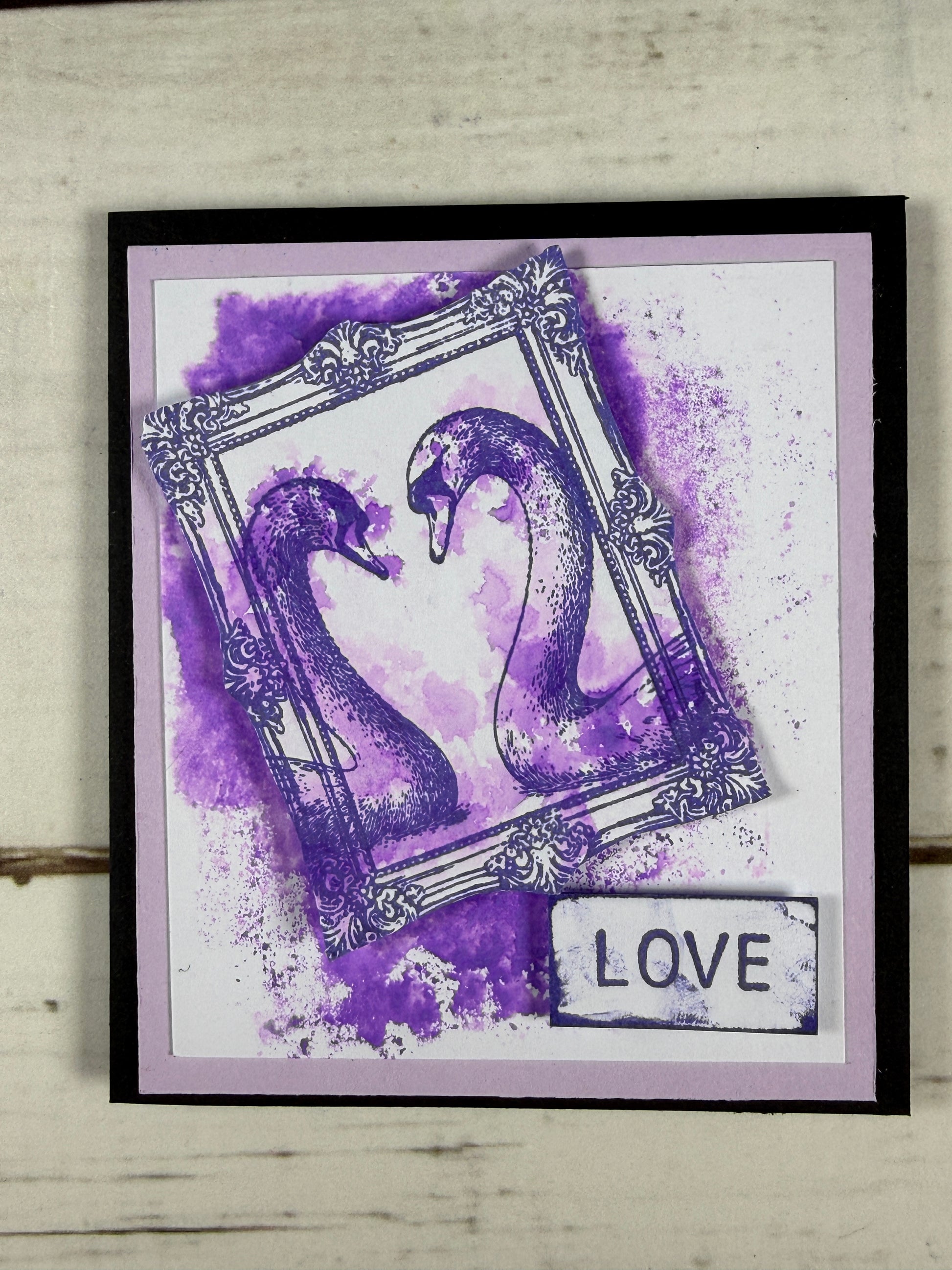 Framed artwork with a purple abstract design and 'LOVE' text on a light wooden surface.