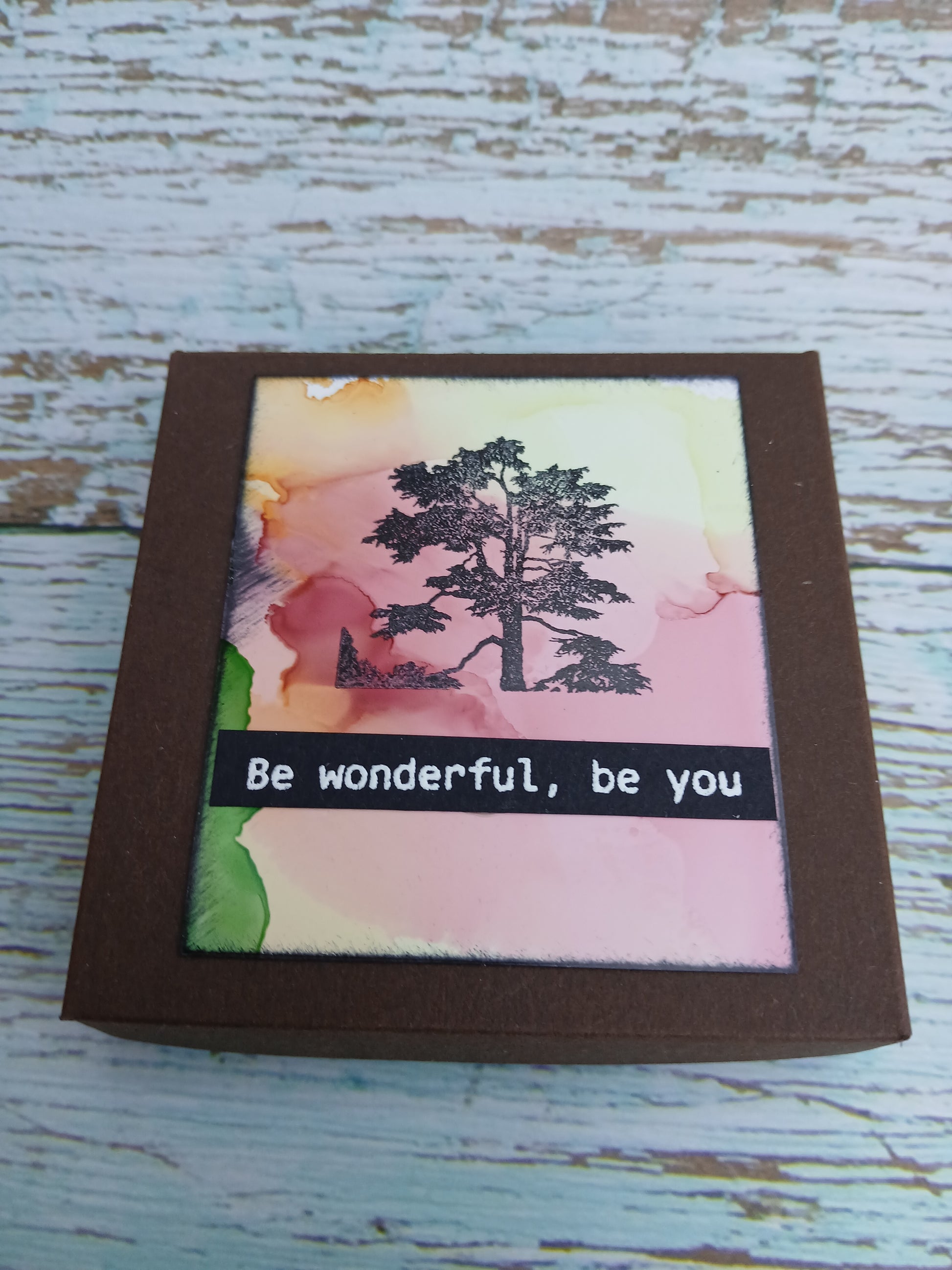 Small framed artwork with a tree illustration and motivational quote on a wooden surface