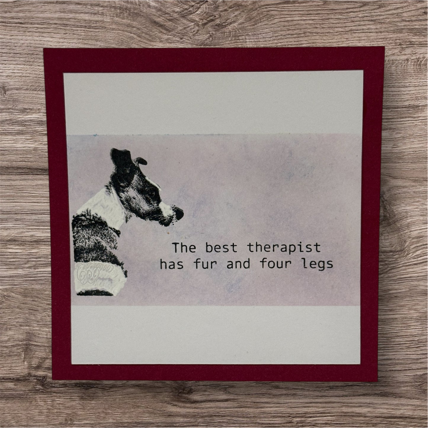 Card with a dog illustration and text 'The best therapist has fur and four legs' on a wooden surface.