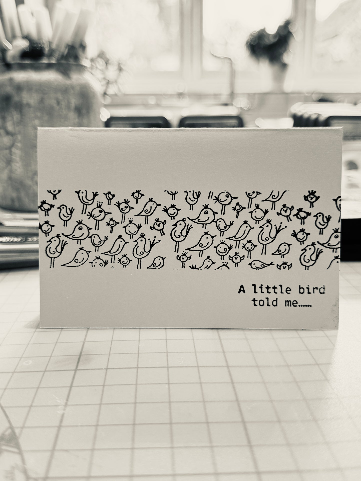 Card with bird pattern and text 'A little bird told me' on a tiled floor background