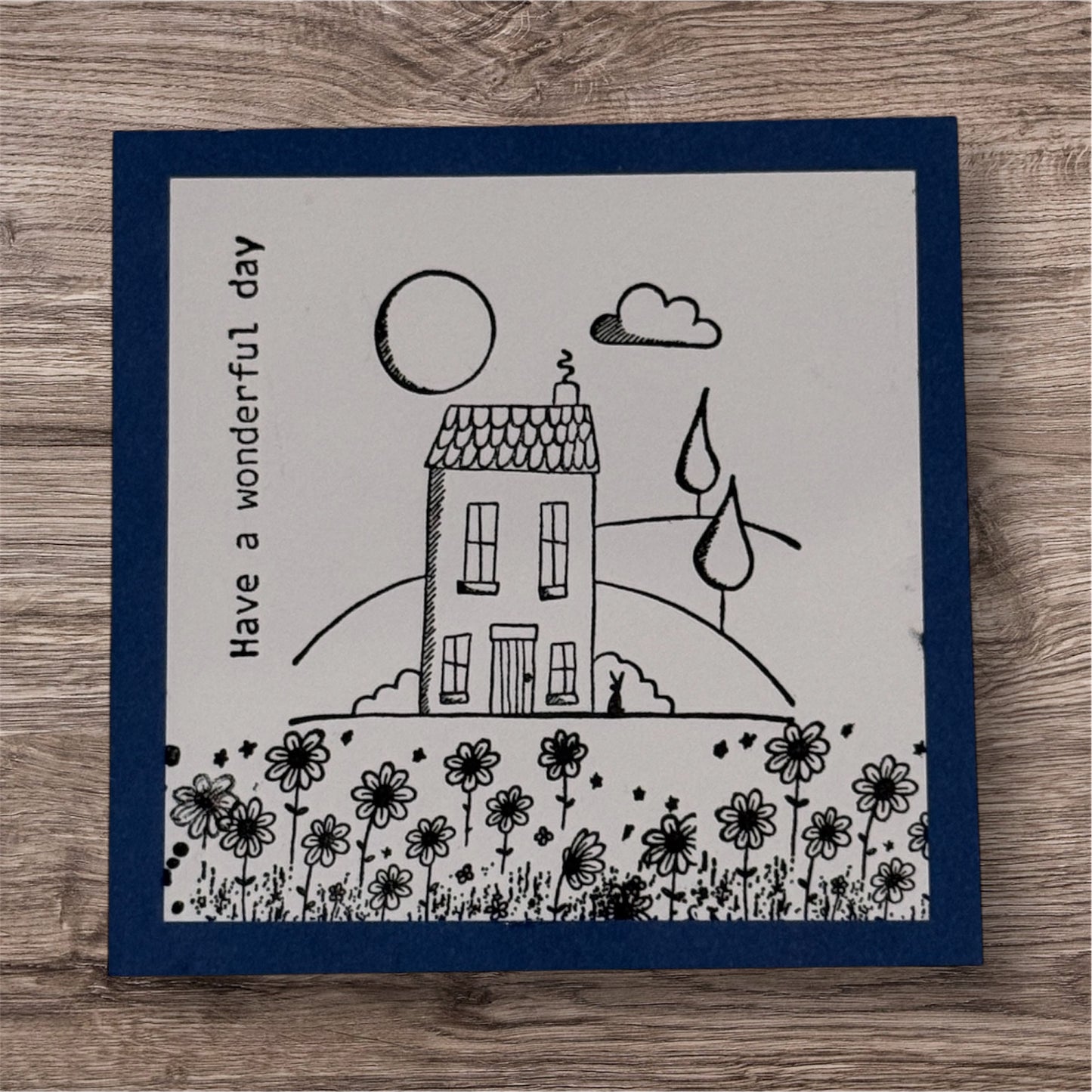 Card with a house, flowers, and 'Have a wonderful day' text on a wooden surface