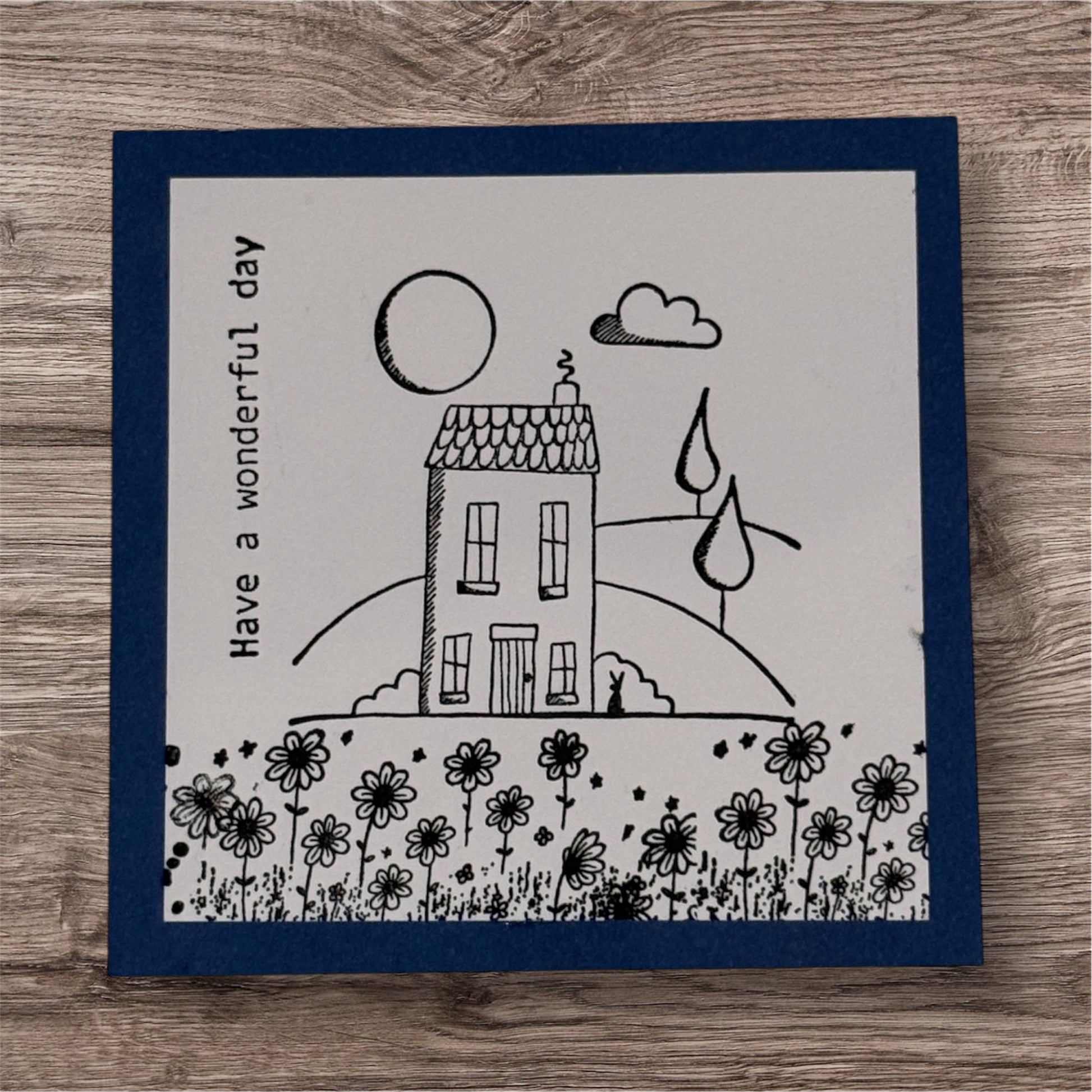 Card with a house, flowers, and 'Have a wonderful day' text on a wooden surface