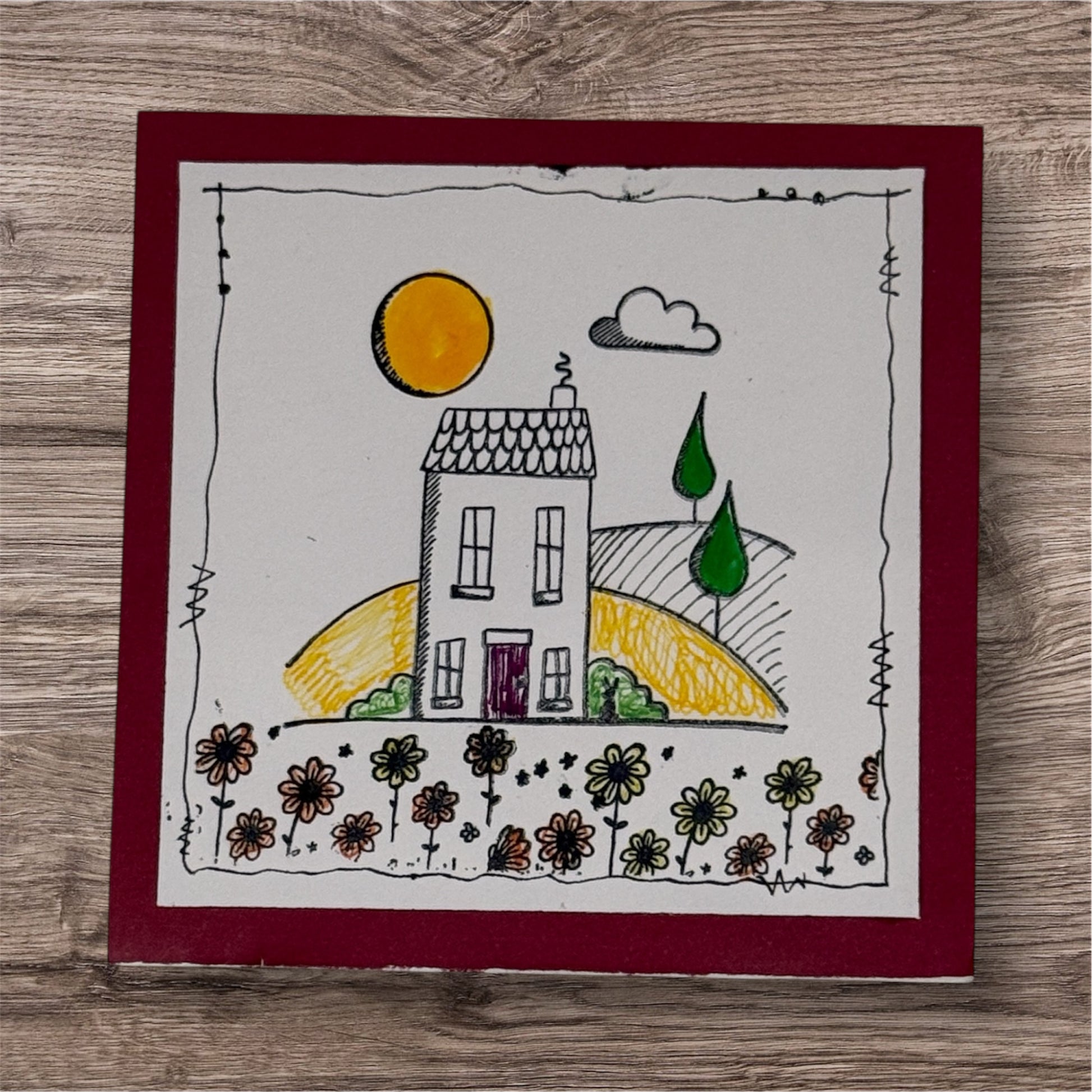 Children's drawing of a house with a sun and flowers on a wooden surface
