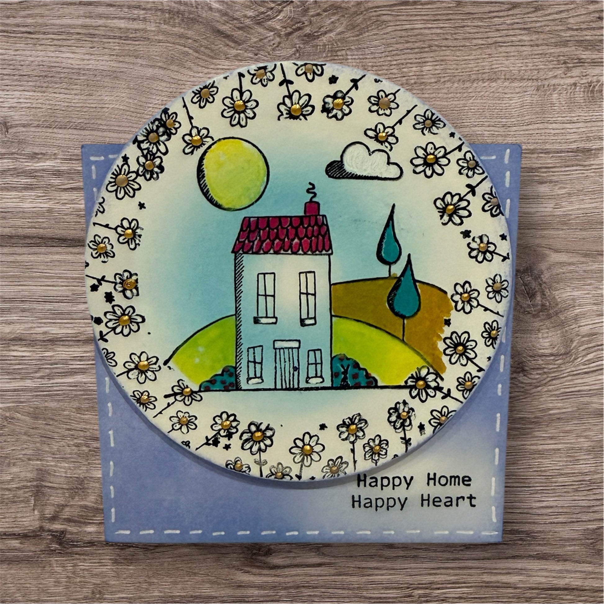 Decorative plate with a house illustration and floral patterns on a wooden surface