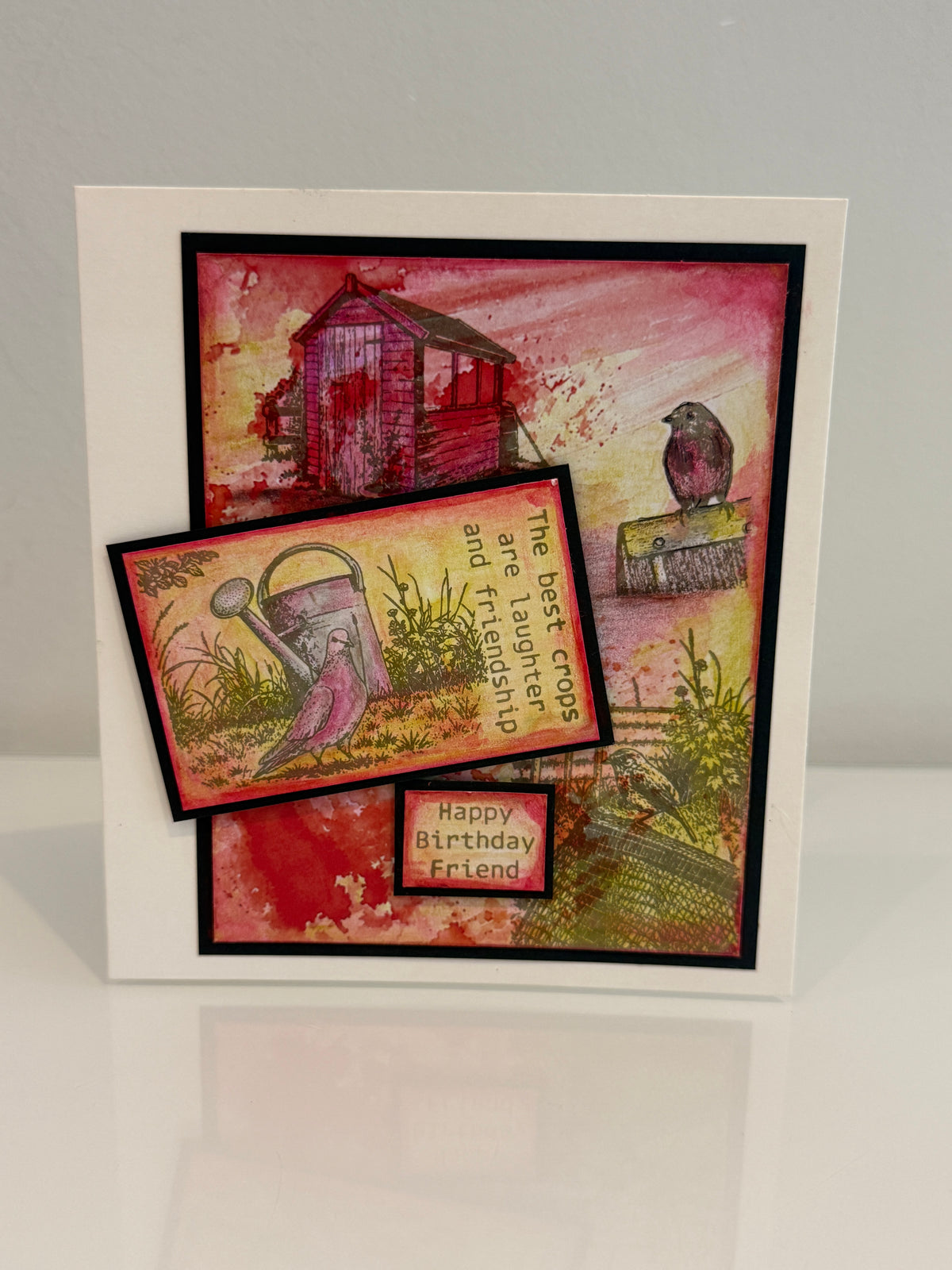 A handmade greeting card with a white border and layered artwork featuring a red shed, a bird, a watering can, and the text 'The best friends are friendship and friendship is the best kind of love. Happy Birthday Friend.