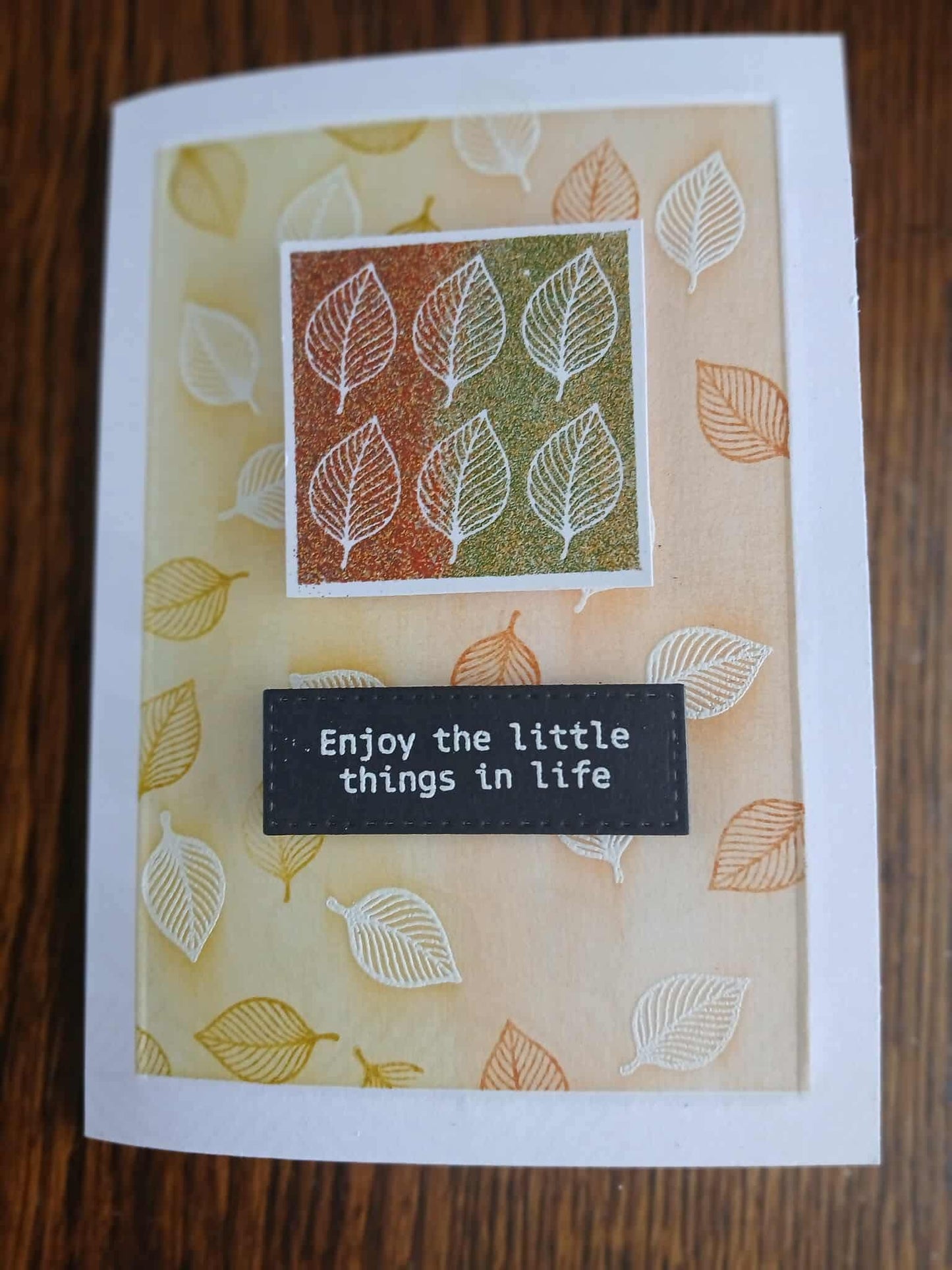 Card with leaf pattern and 'Enjoy the little things in life' text on a wooden surface